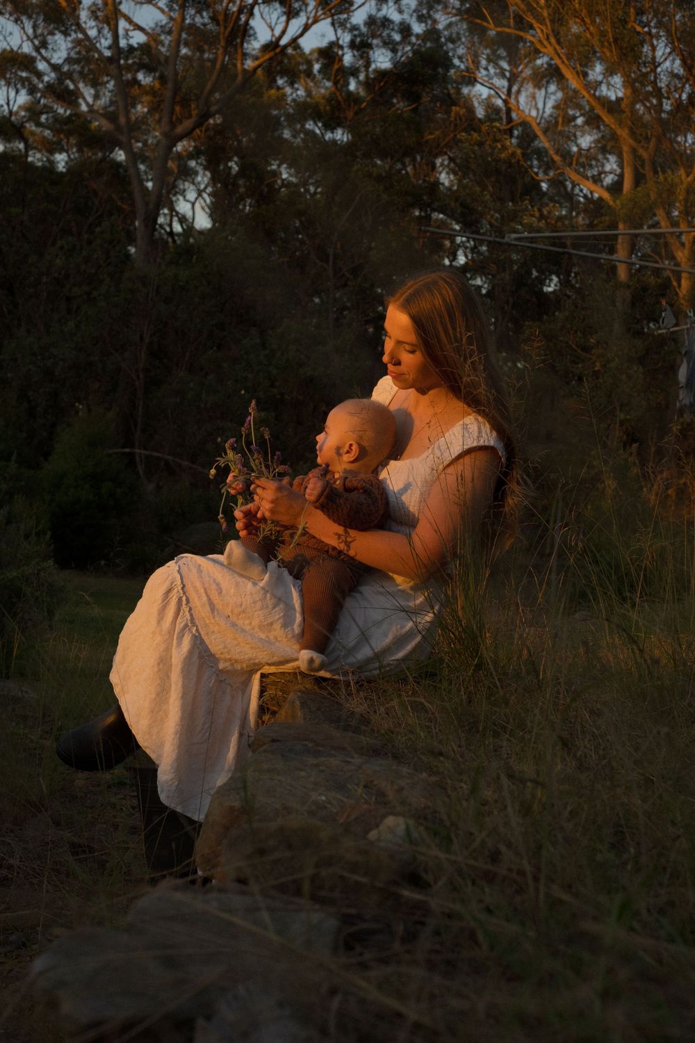 Peaceful outdoor portrait of parent and child sitting with wildflowers at golden hour.