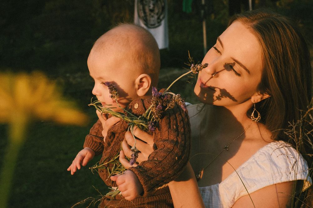 Mother and baby share tender moment outdoors in golden sunlight with wildflowers.