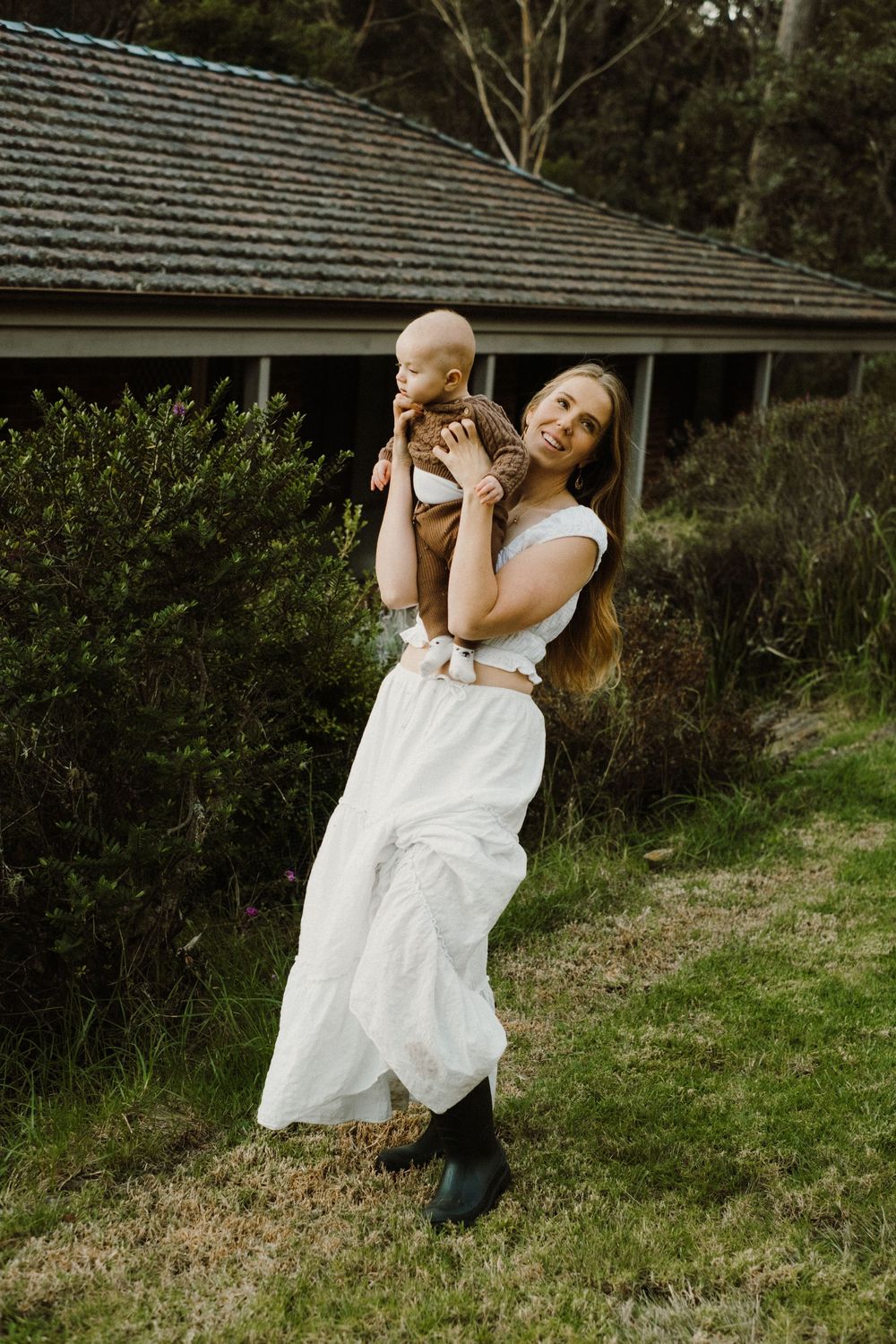 Dancing movement captured in white dress against rustic house backdrop.