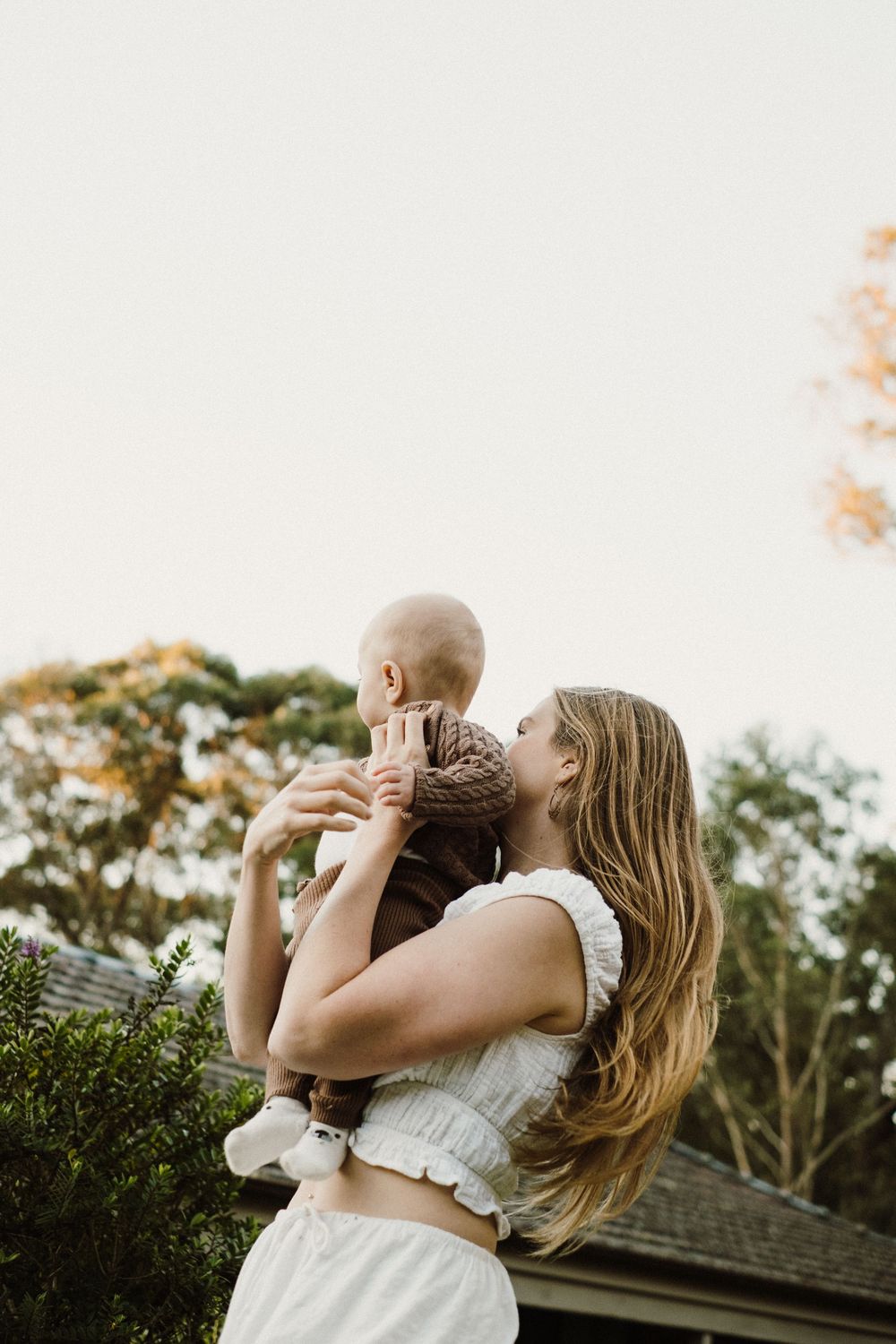 Tender moment captured in natural outdoor setting with white dress against greenery.
