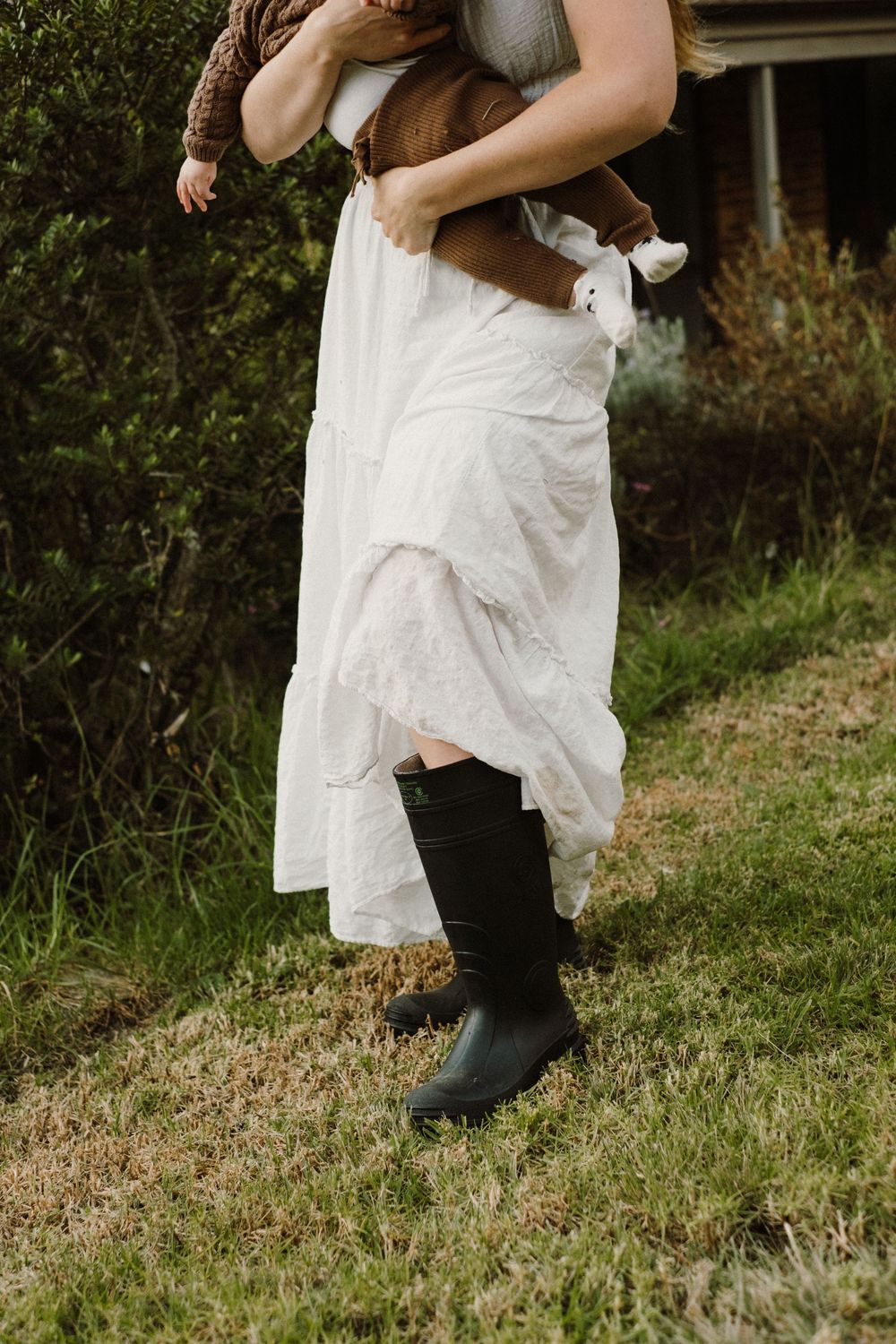 Close-up view of white dress and black boots on grassy ground against natural outdoor backdrop.