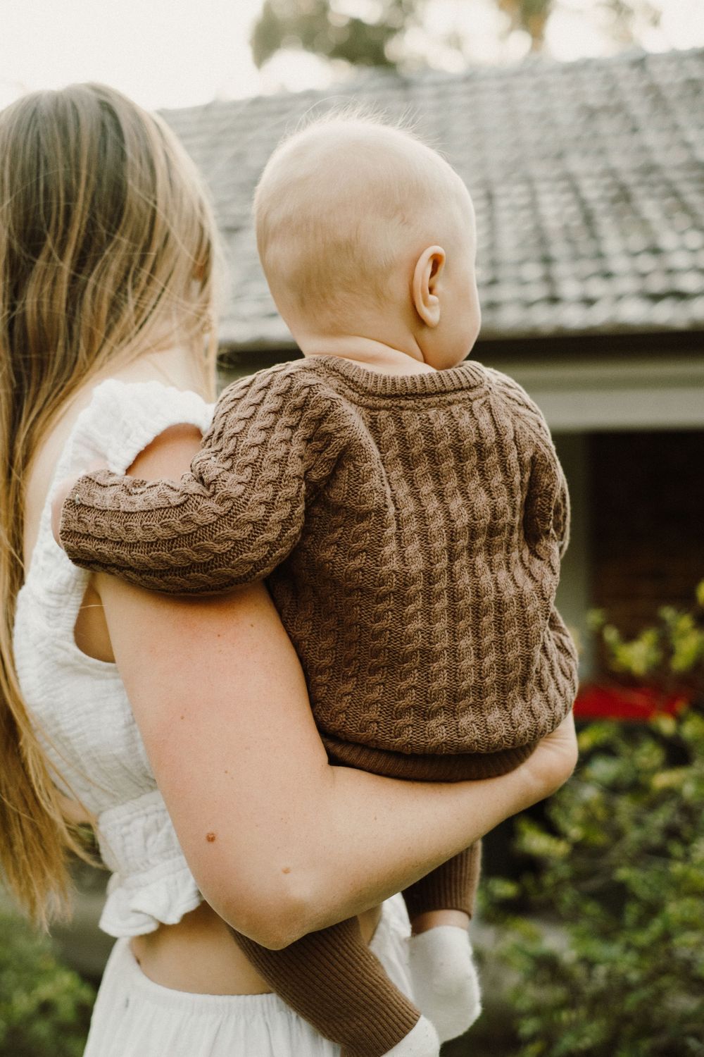 Close-up of brown cable knit sweater against outdoor garden setting.