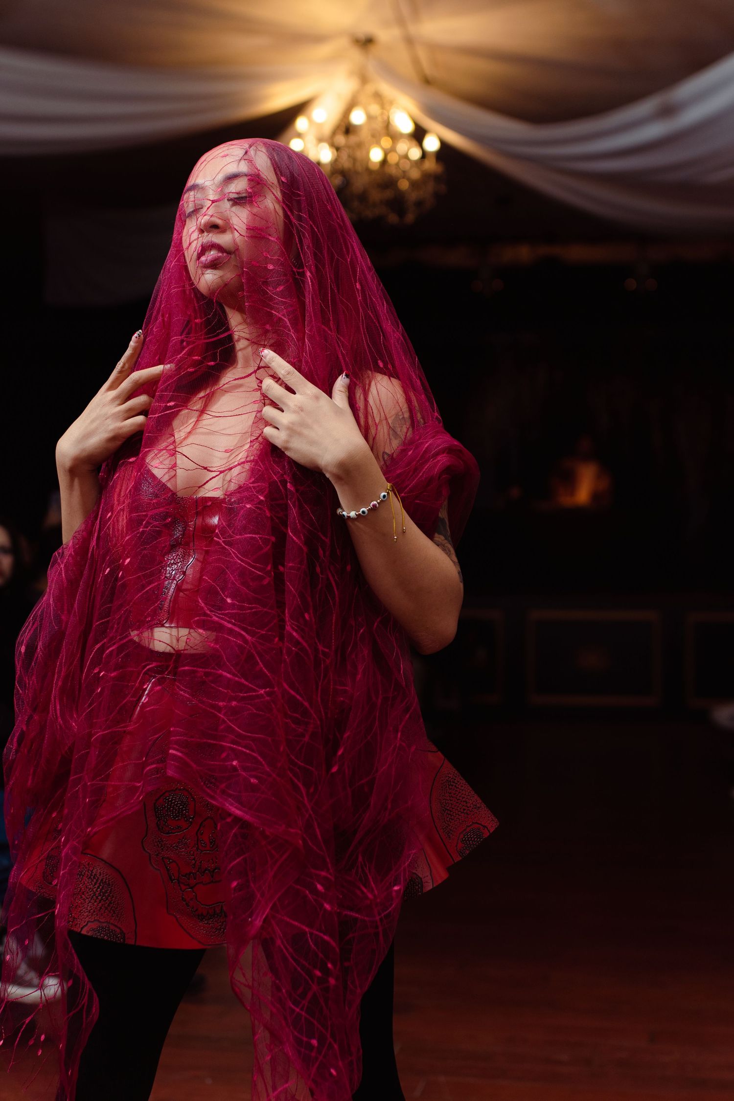 Dramatic fashion shot of dancer in flowing red veil under chandelier lighting.