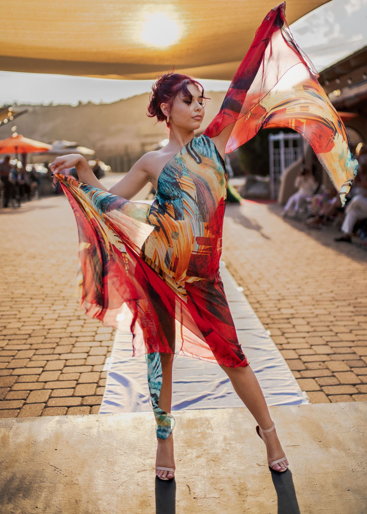 Dancer performs in vibrant printed dress against sunset at outdoor venue.