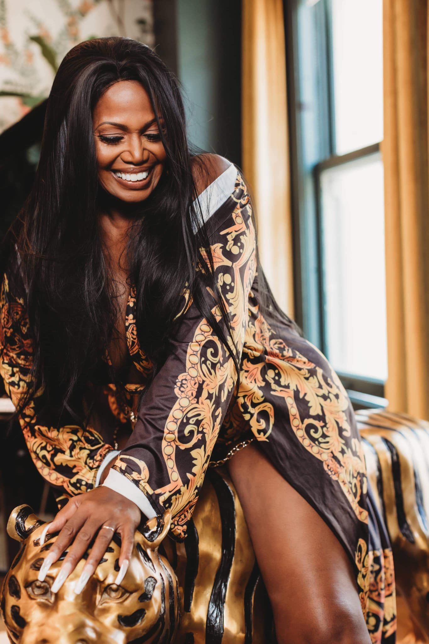 Woman in patterned dress laughing by window with natural sunlight.