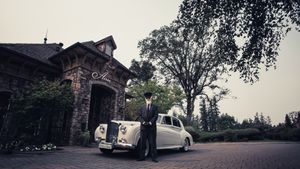 Vintage Rolls Royce parked in front of stone mansion on overcast day.