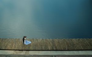 A photographer silhouetted against a dark sky captures a shot while standing on a stone wall by the water.