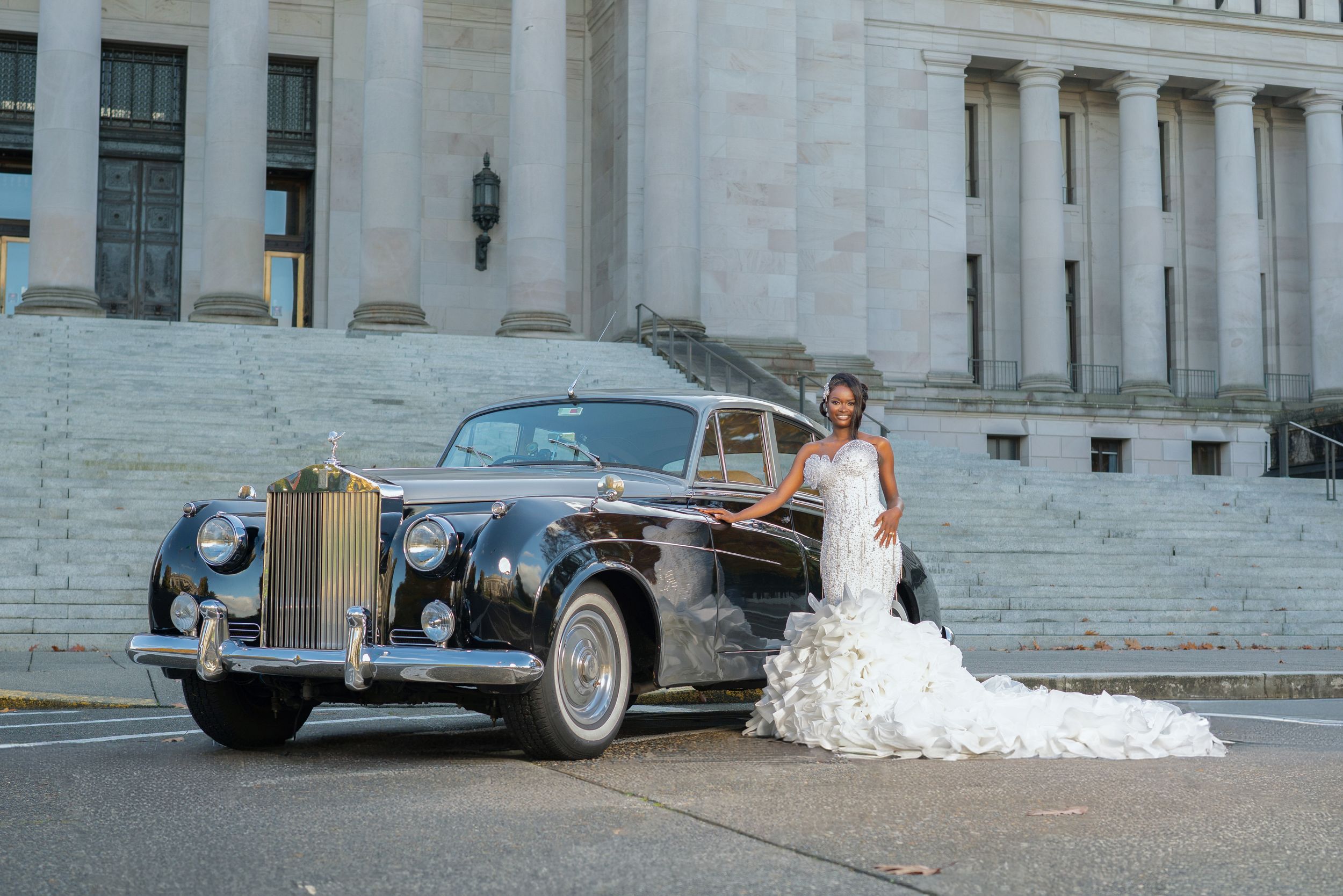 Wedding party with classic cars arranged along stone steps of an elegant building facade.