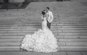 A black and white panoramic sequence shows a bride in a flowing white gown descending stone steps outdoors.