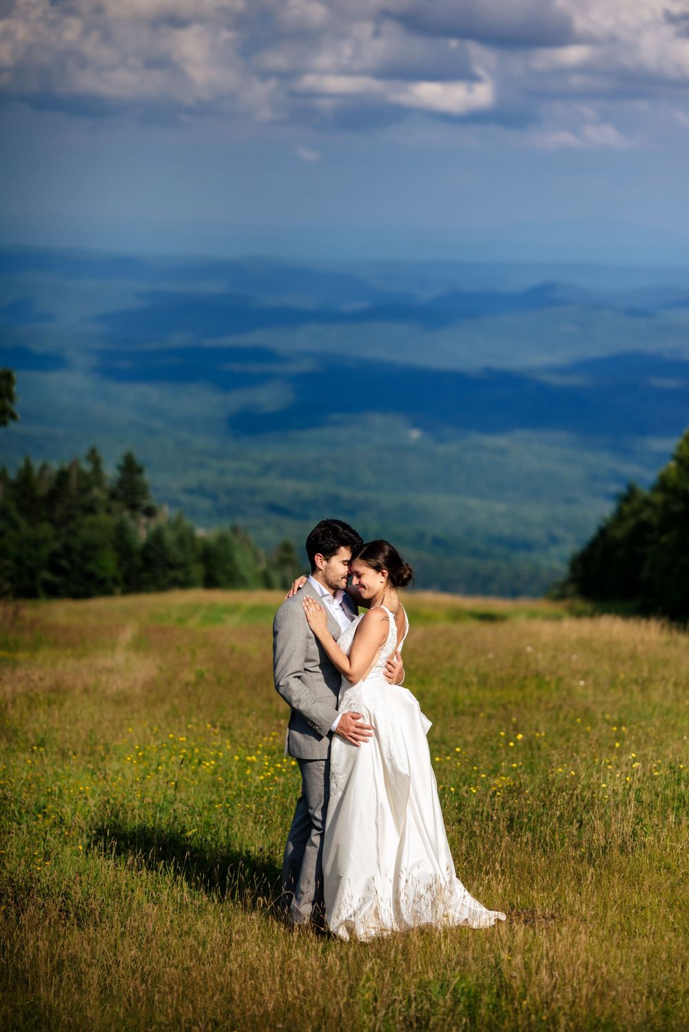 Bride and groom embracing in a mountain meadow with stunning blue ridge views on their wedding day.