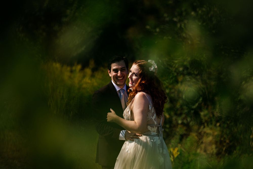 Bride and groom sharing a romantic moment framed by lush green foliage in a garden setting.