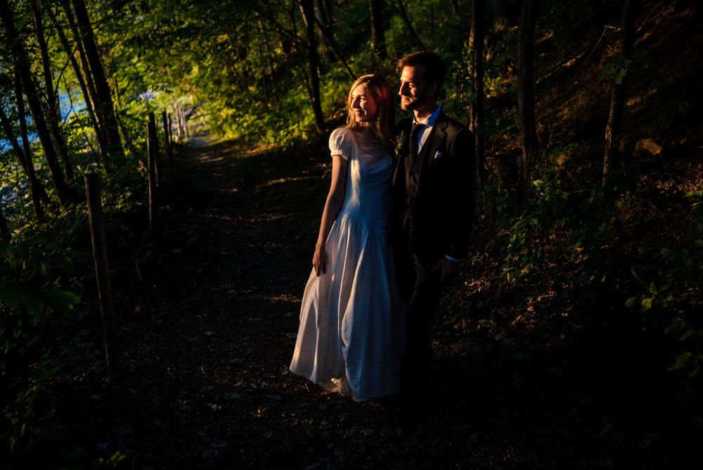 Newlyweds walking hand in hand down a sunlit forest path in elegant wedding attire at golden hour.