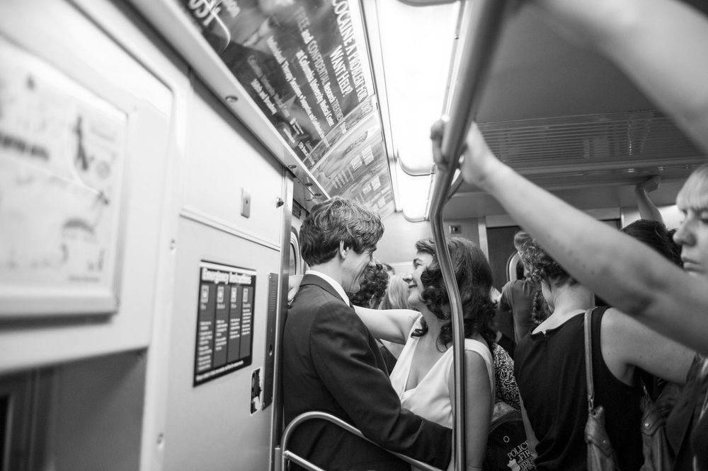 Bride and groom ride subway train together in black and white candid wedding photo.