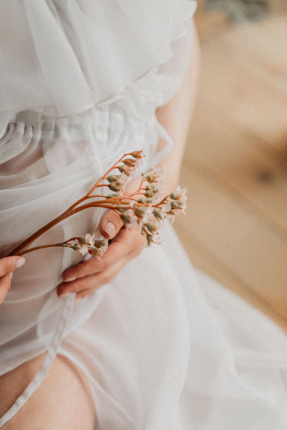 Delicate close-up of hands holding dried flowers against flowing white fabric.