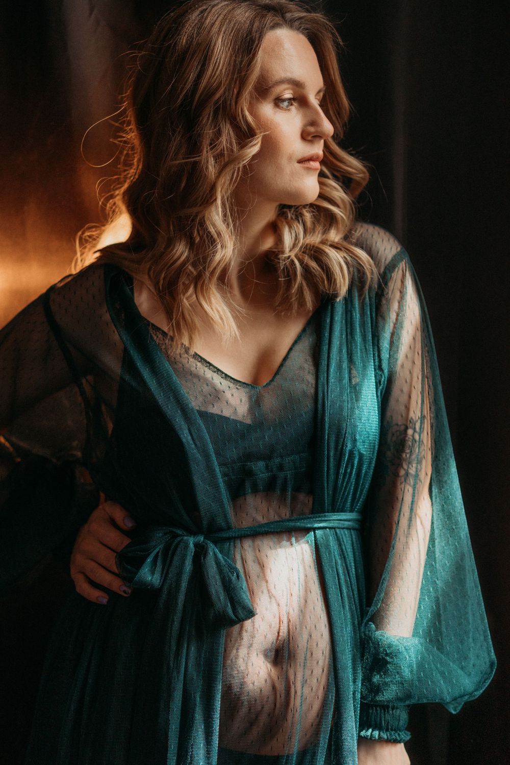 Artistic boudoir portrait with teal flowing fabric against dark background.