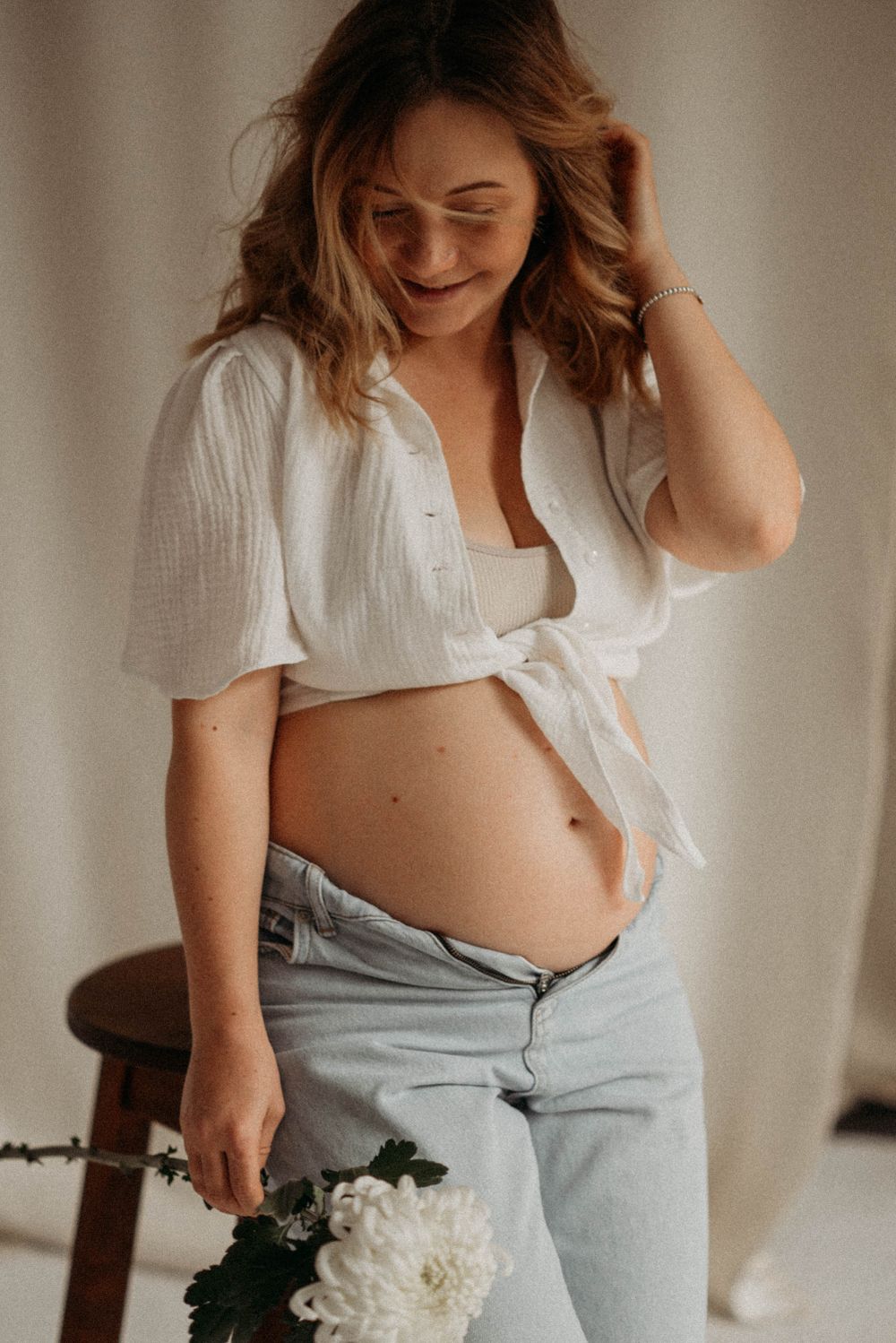 Casual maternity photos in white top and jeans holding white flowers.