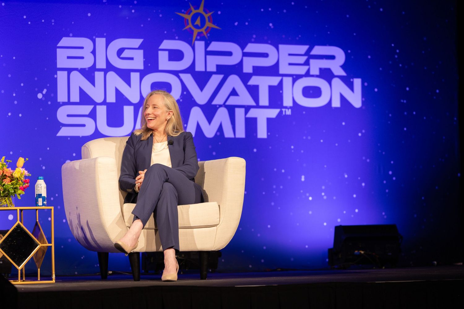 Woman in navy suit seated on stage speaking at the Big Dipper Innovation Summit conference event.