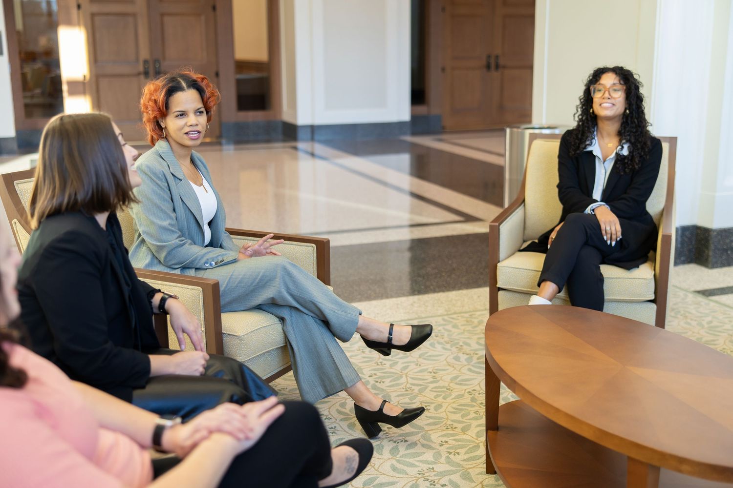 Business professionals seated in a formal meeting room with wooden furniture and white walls.