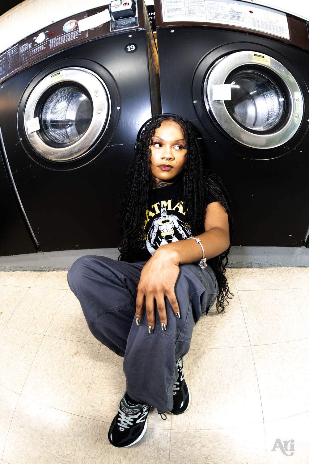 Person sitting against industrial washing machines in casual streetwear.