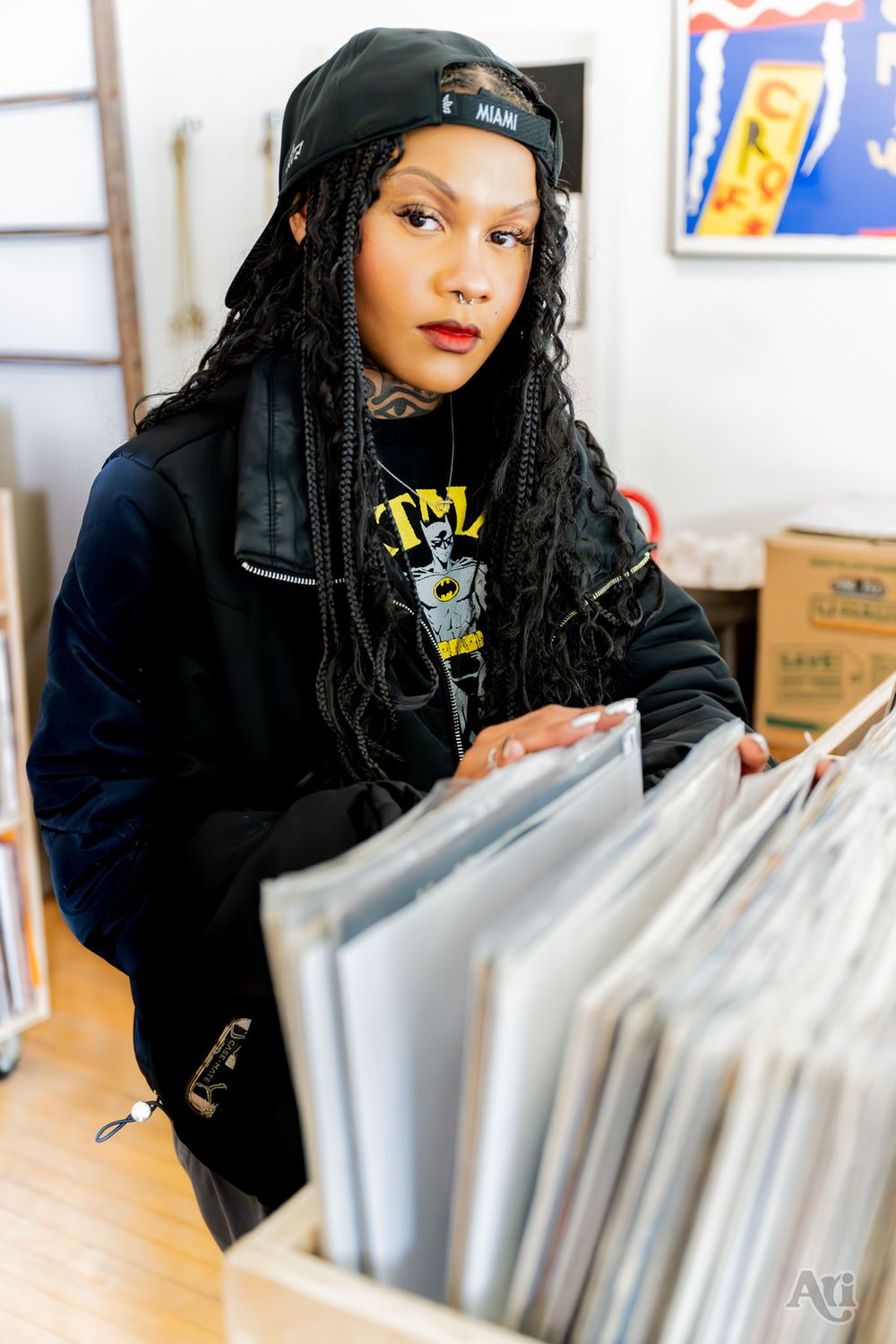 Person browsing vinyl records wearing black hat and jacket in record store.