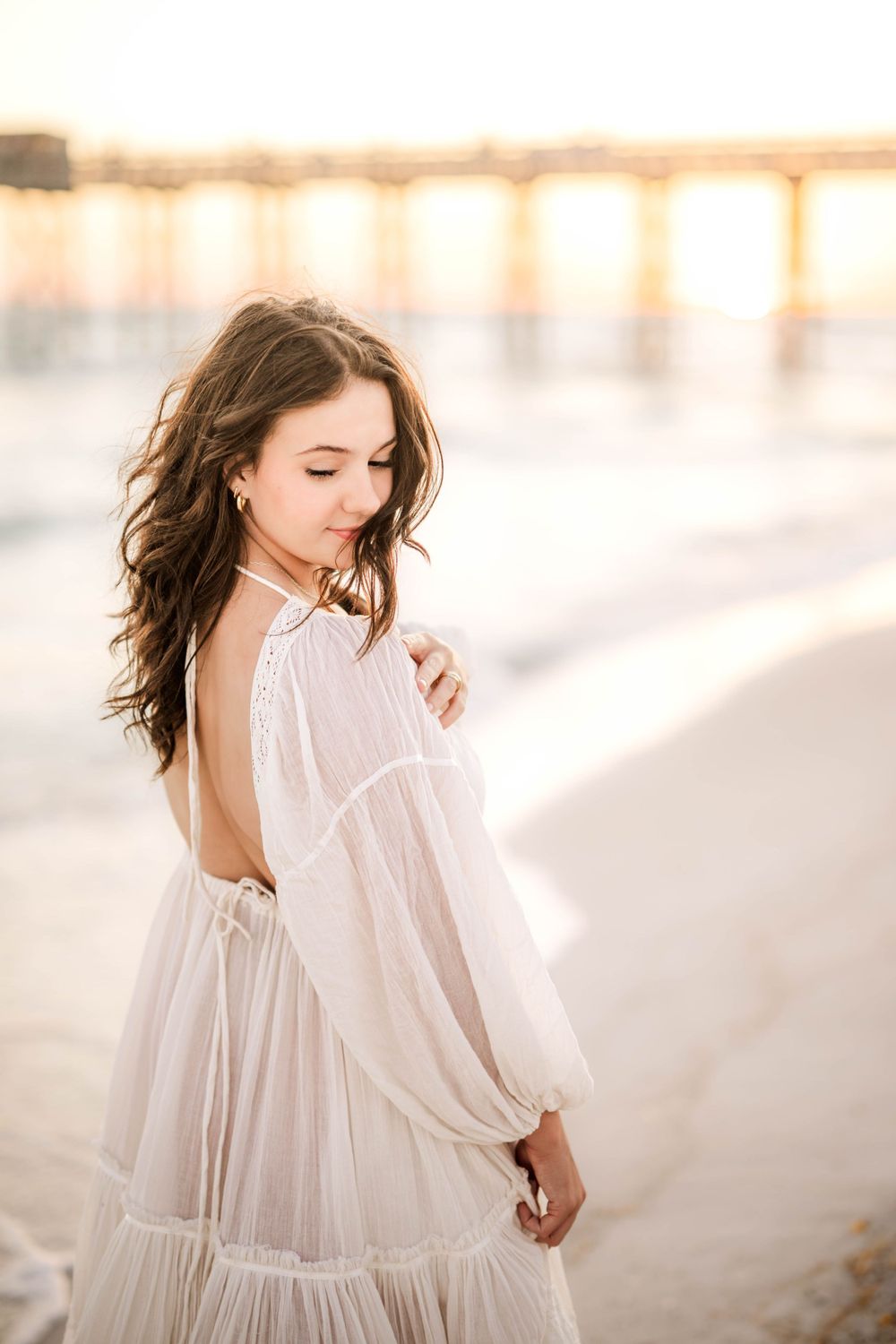 Dreamy backlit portrait in a white flowy dress against soft coastal lighting.