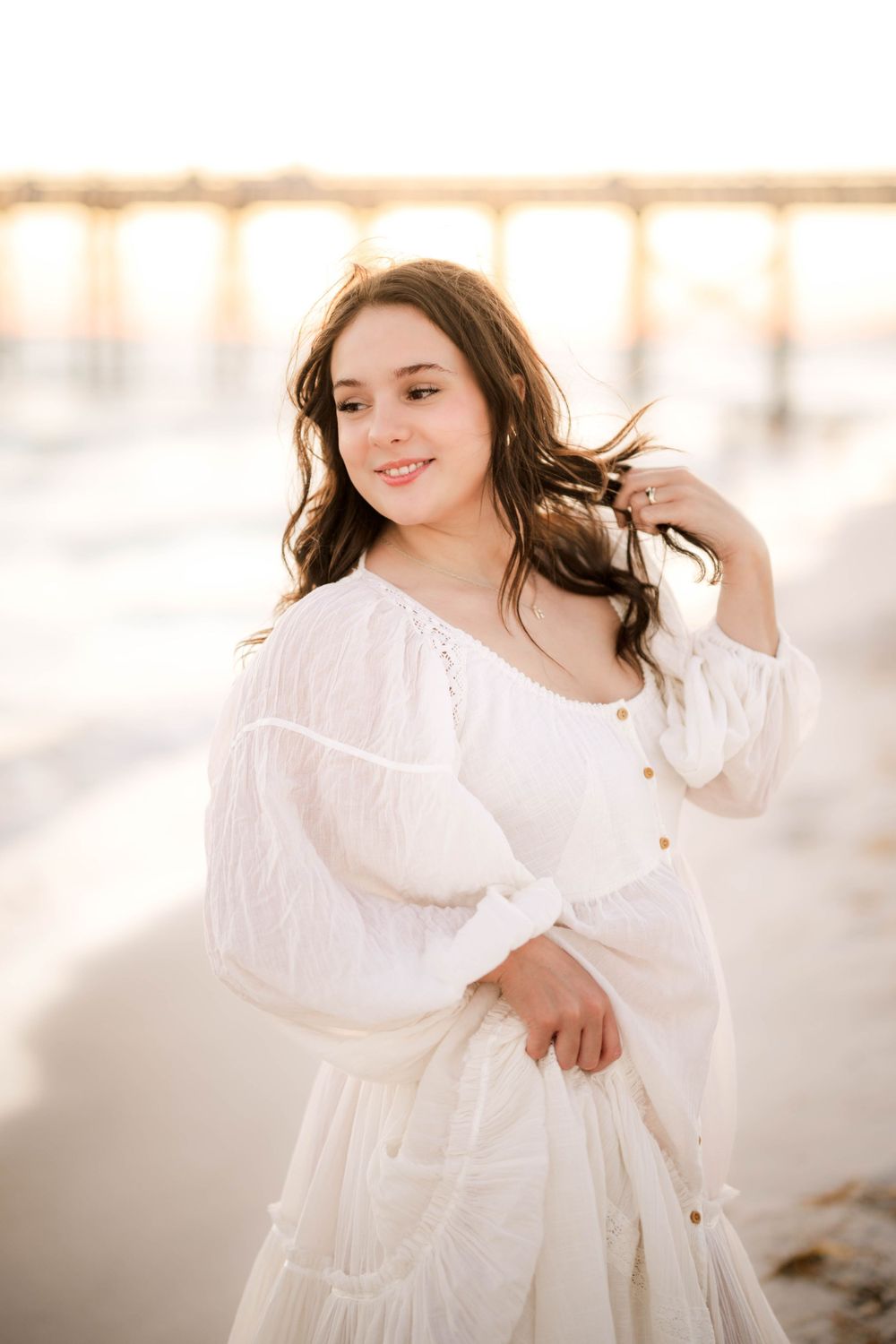 Carefree beach portrait in billowy white dress with golden hour lighting.