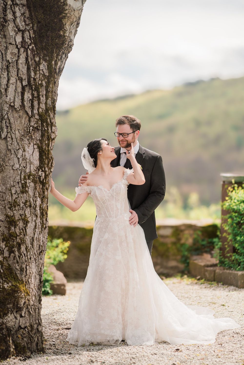Newlyweds share intimate moment while posing by large tree trunk in scenic location.