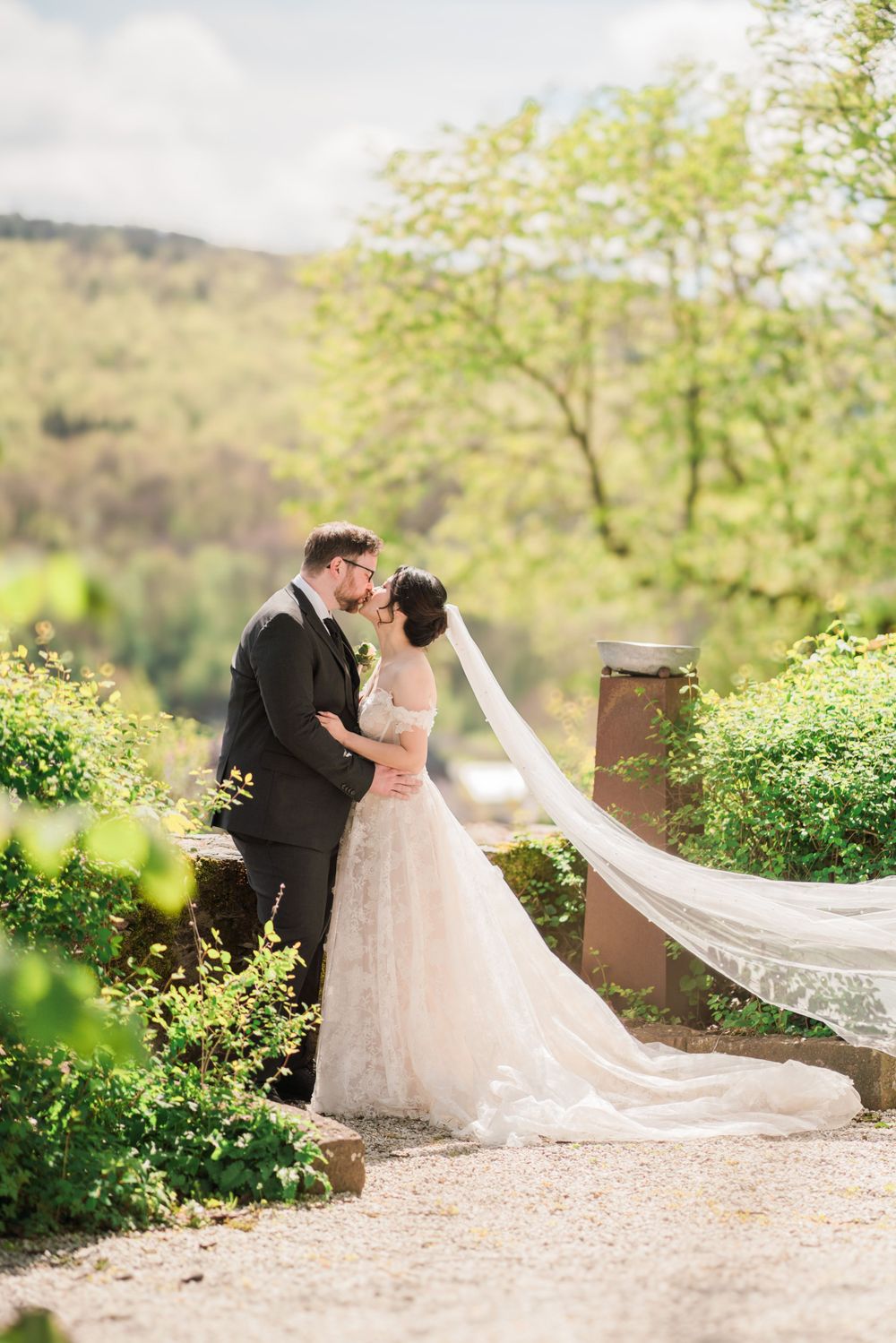 Romantic wedding portrait with flowing veil against scenic mountain backdrop.