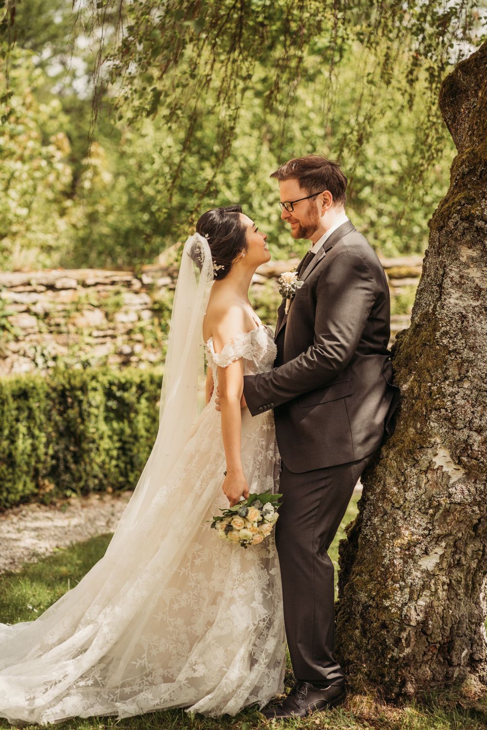 Intimate wedding portrait of couple beside large tree trunk in garden setting.