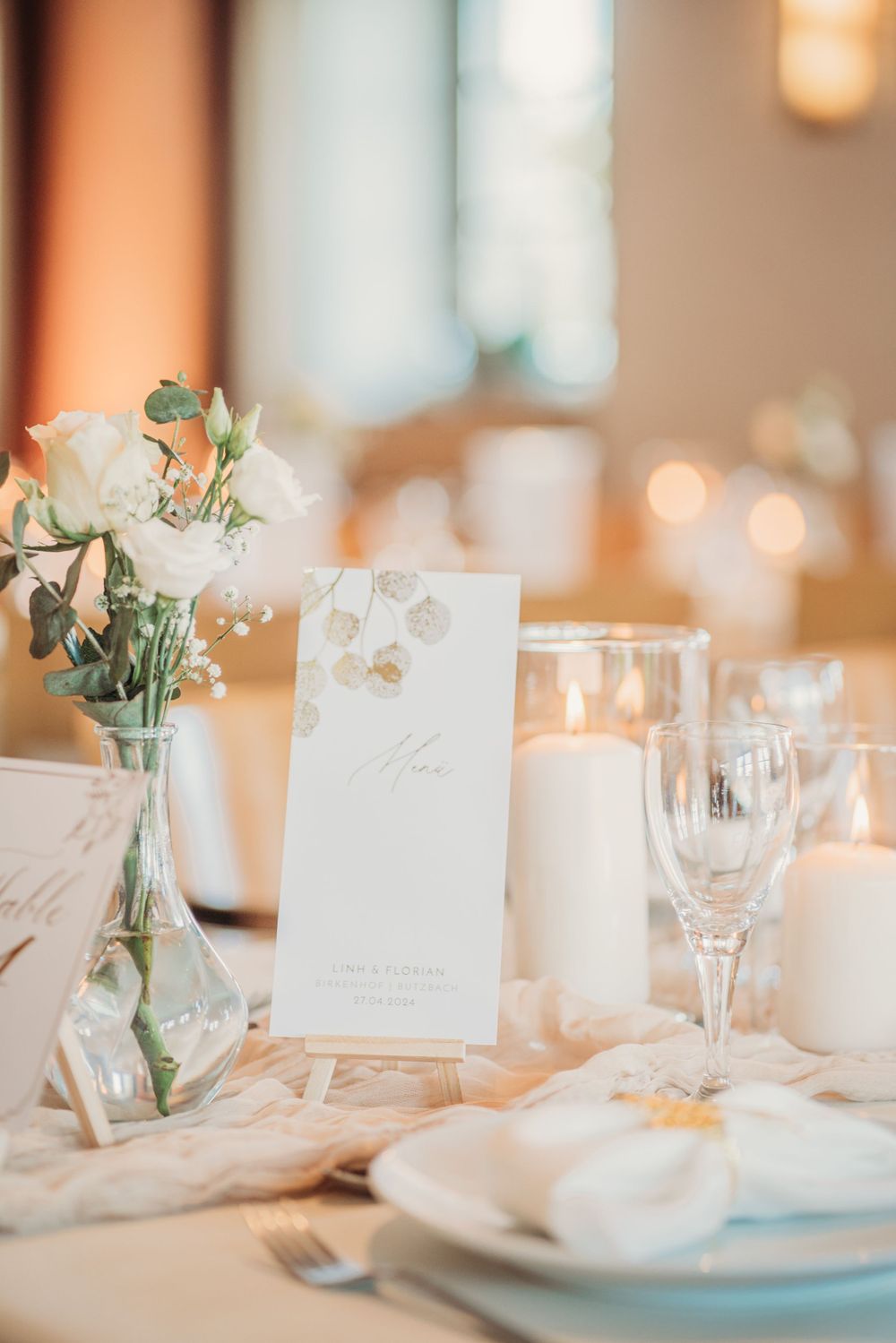 Romantic table setting with white menu card, floral centerpiece, and candlelight creating soft ambiance.