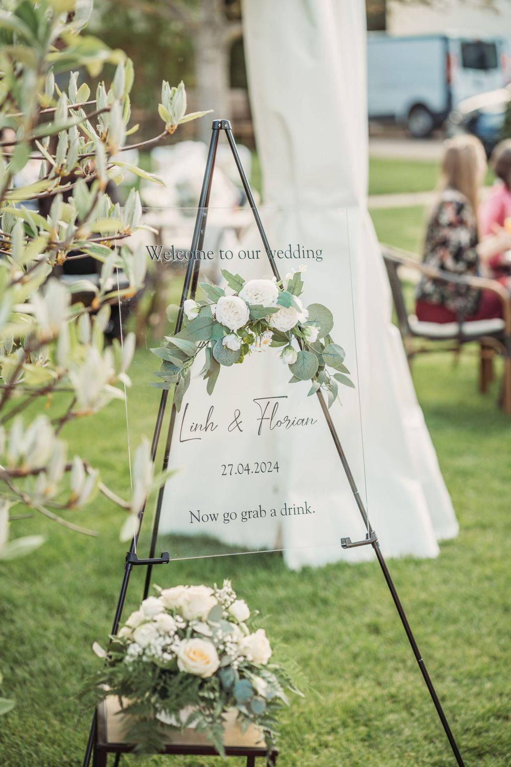 Welcome wedding sign displayed on easel with white floral decorations in an outdoor garden setting.