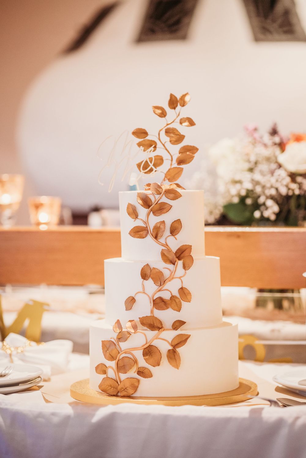 Elegant white wedding cake decorated with intricate copper-colored leaf design.
