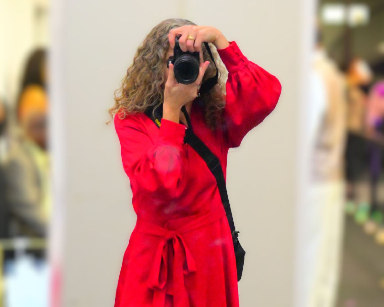 The photographer wearing a red dress captured in the mirror as a self portrait with her face obscured by the camera.