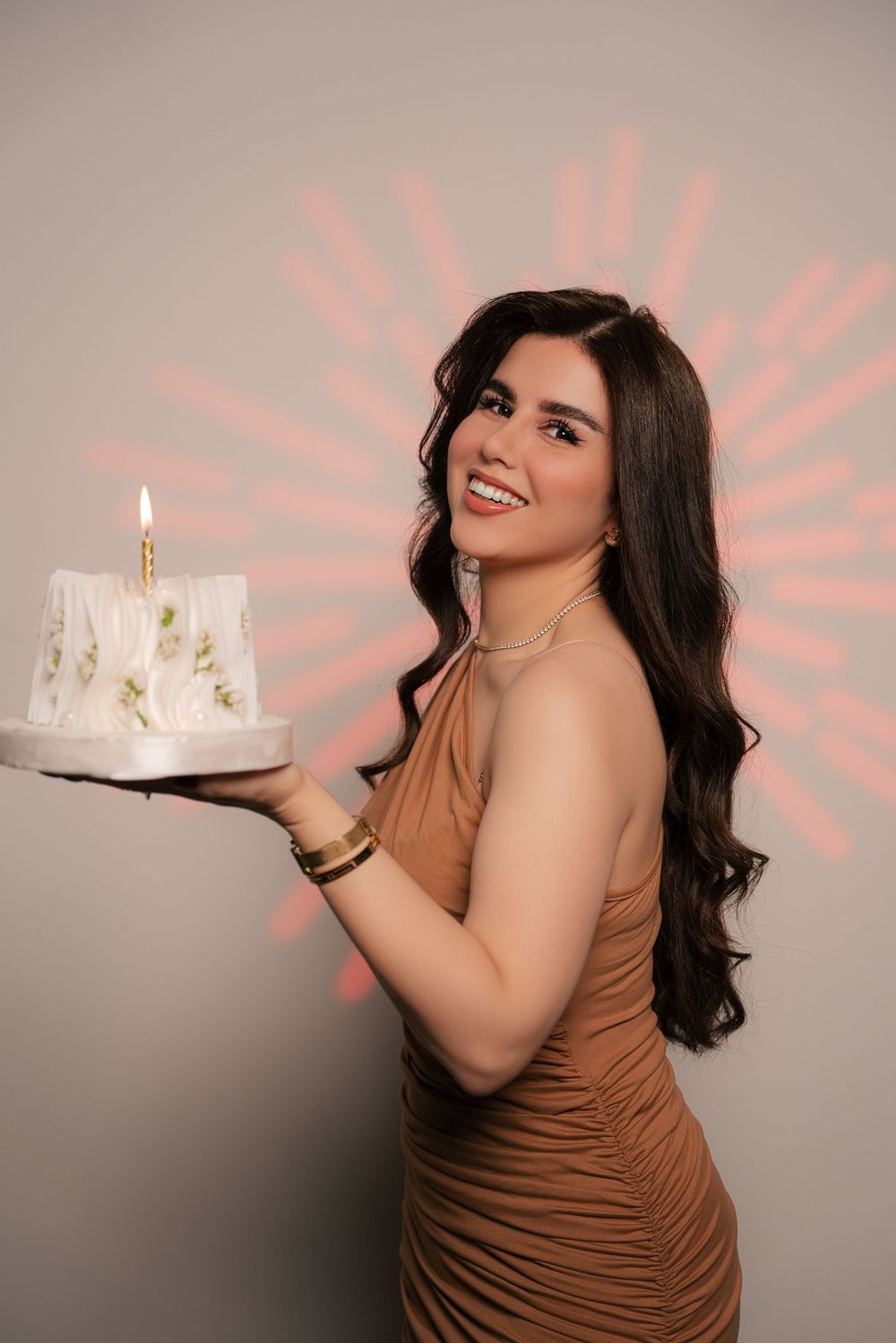 A sequence of photos shows someone in a brown dress posing with a lit birthday cake against a gray backdrop.