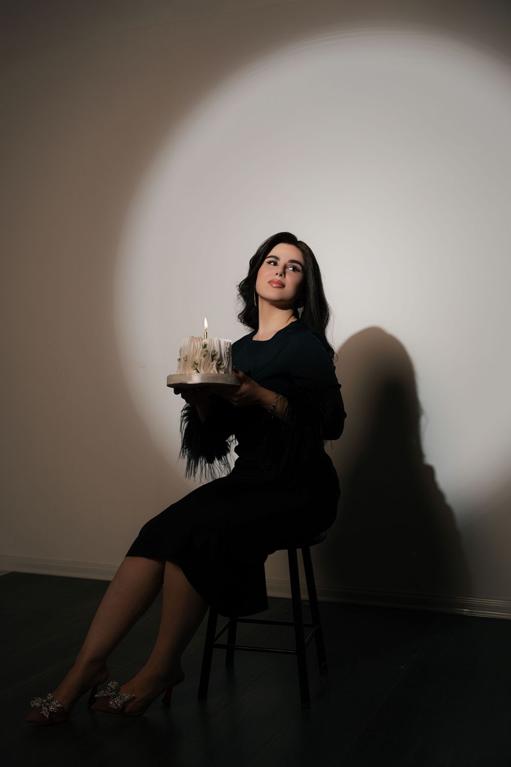 A dramatic black and white photo series showing a person in dark clothing posing on a chair against a shadowy wall.