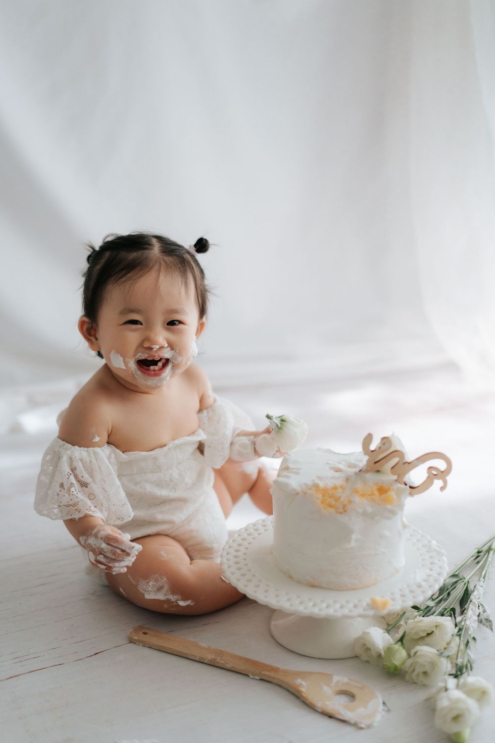 A cake smash photo session featuring a white cake and floral decorations on a light backdrop.