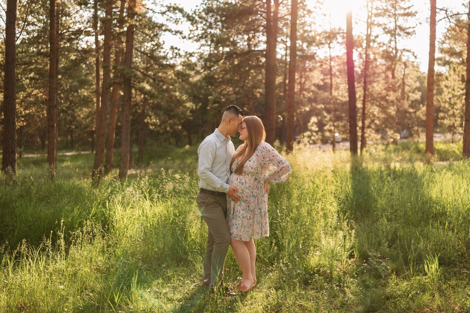 Couple embraces in golden sunlit forest clearing during sunset with tall pine trees in background. Fox Run Park, Colorado Springs