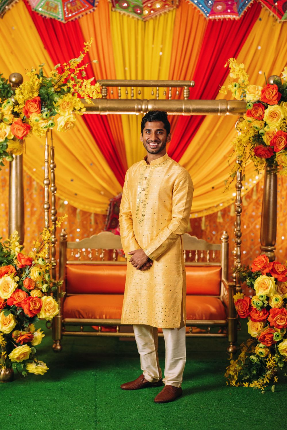 Traditional Indian wedding stage decorated with vibrant yellow and red drapes and colorful floral arrangements.