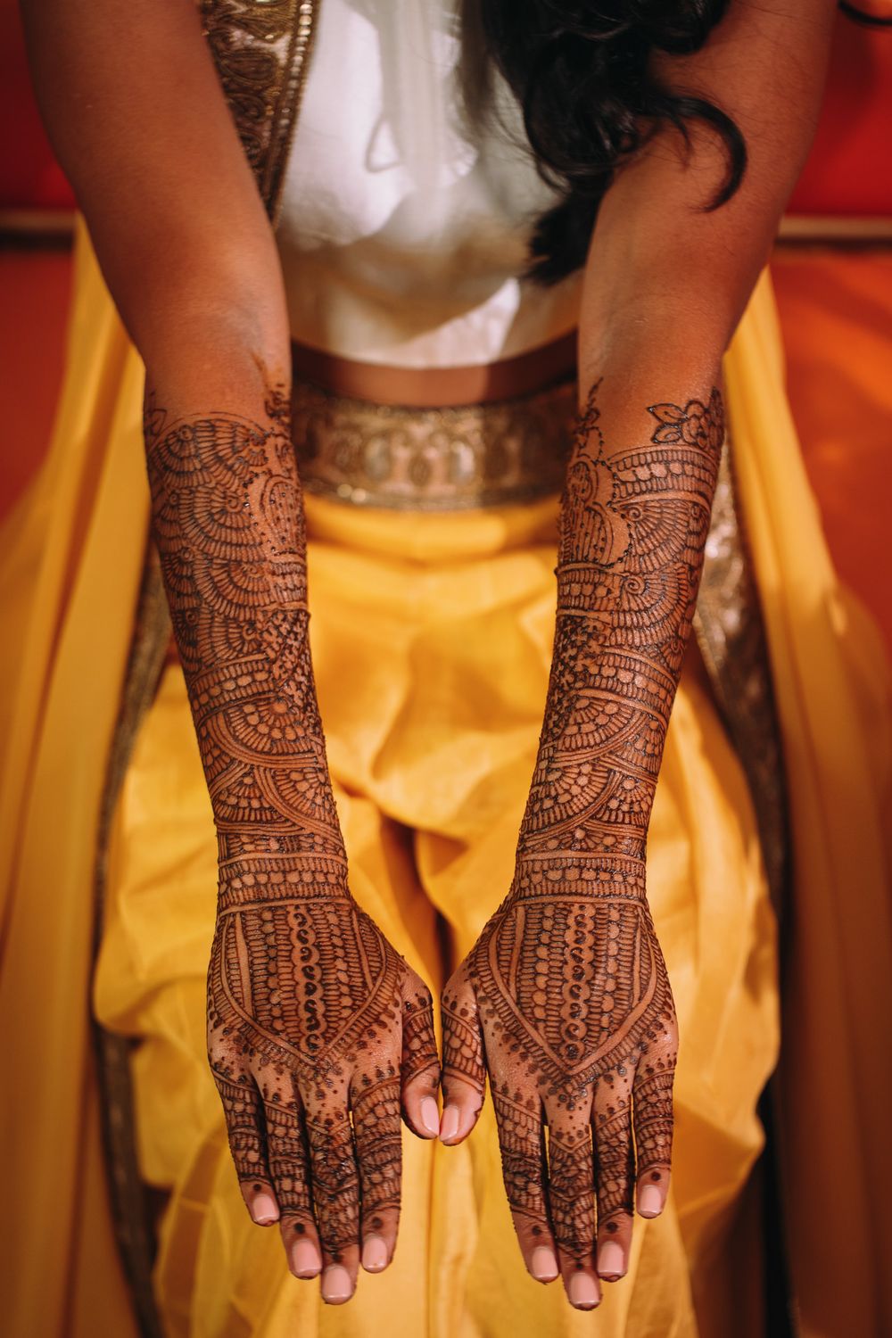 Intricate henna mehndi designs adorning hands against yellow fabric background.