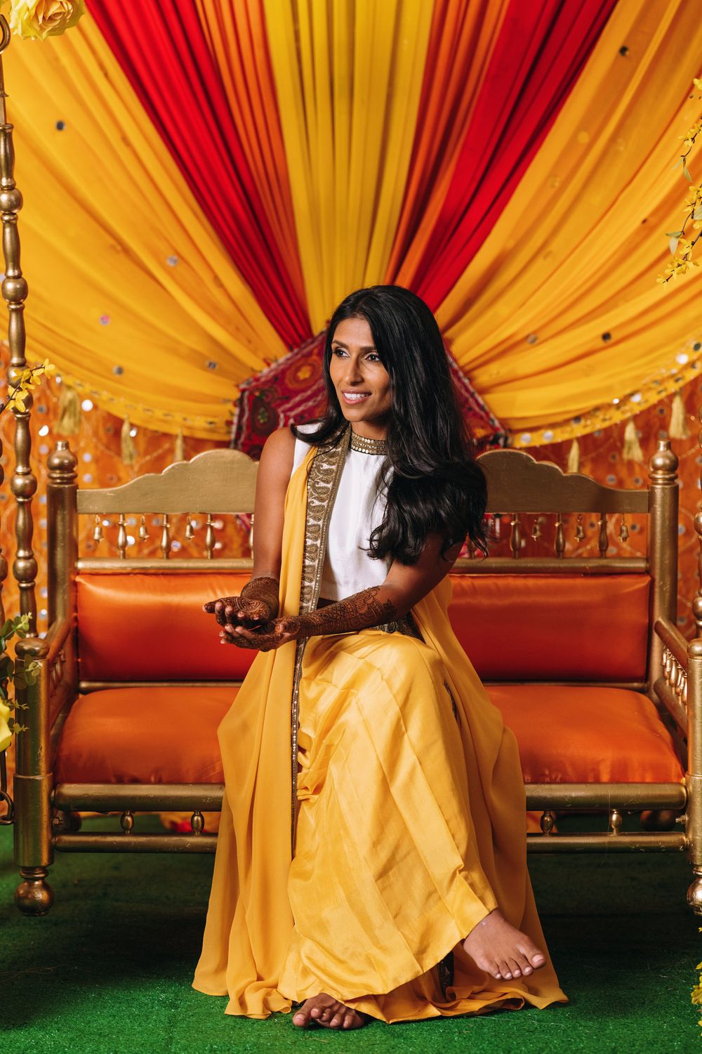 Traditional Indian wedding decor with yellow and red draped fabric backdrop and ornate wooden swing with orange cushions.