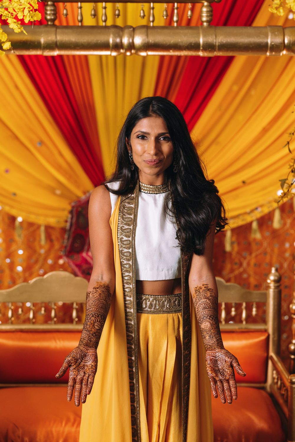 Intricate henna designs adorn hands against a backdrop of red and gold decorative fabric at an Indian wedding ceremony.