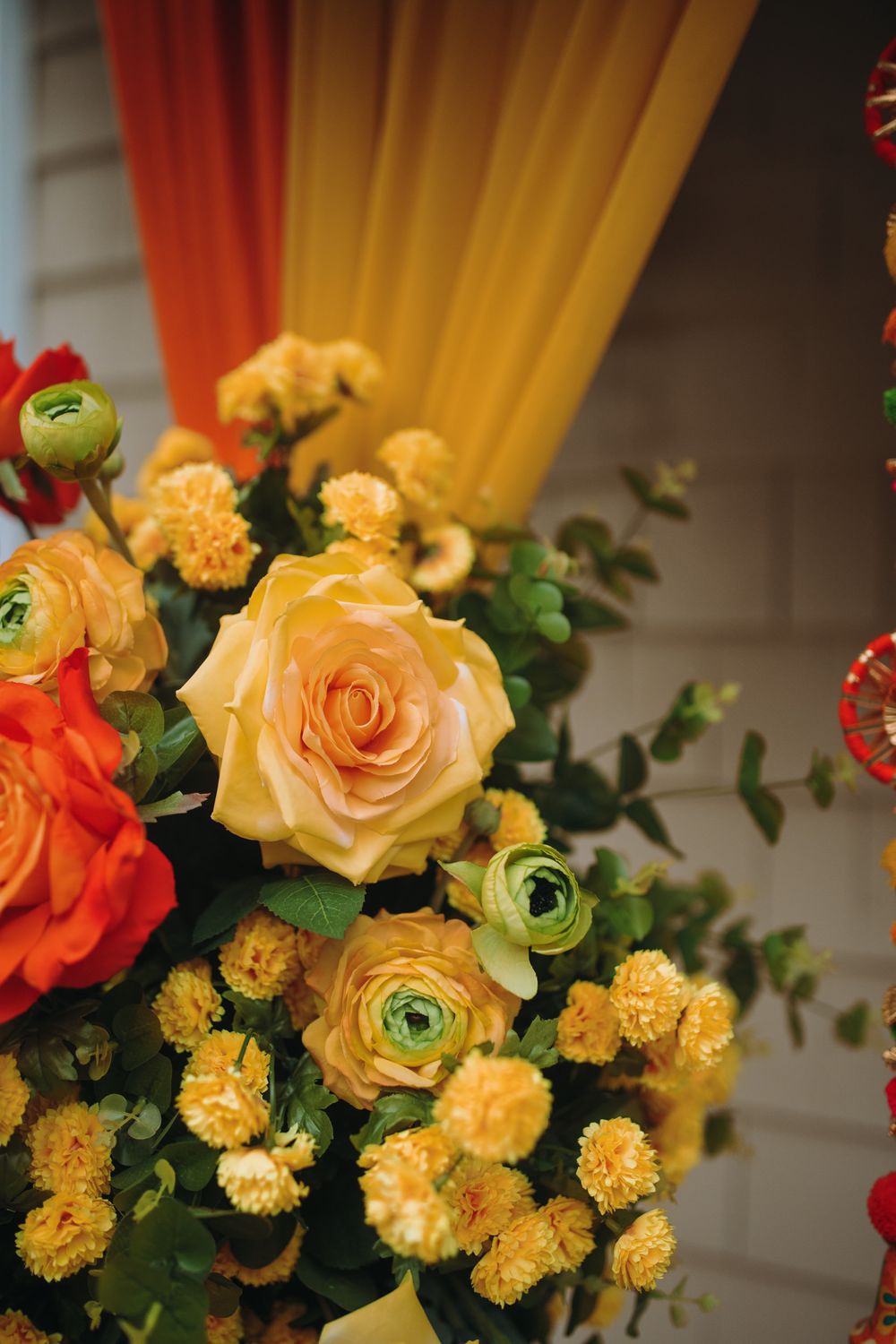 Elegant yellow roses and orange flowers arranged in a decorative display with green foliage.