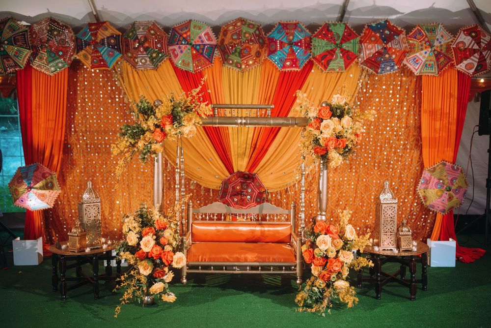 Wedding mandap decorated in orange and gold with floral arrangements.