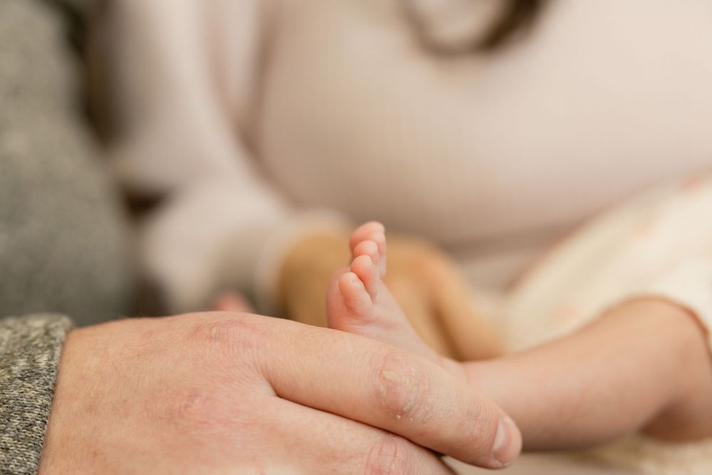 Tiny newborn baby feet being gently held by caring hands against a soft beige background.