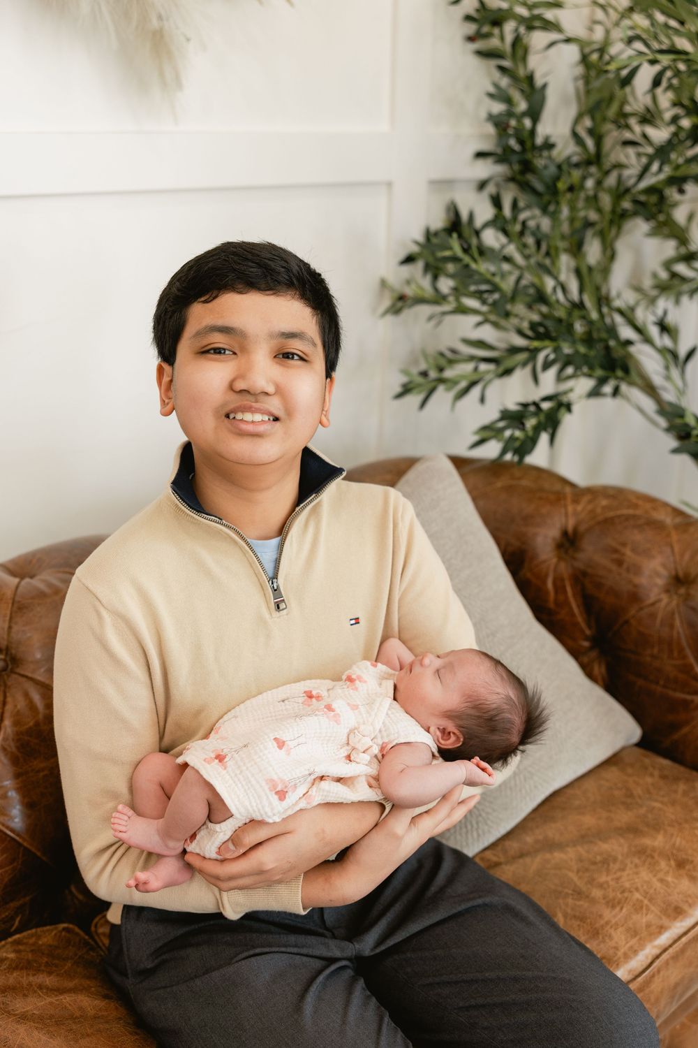 A newborn baby wearing a pink and white outfit rests peacefully on a brown leather couch.