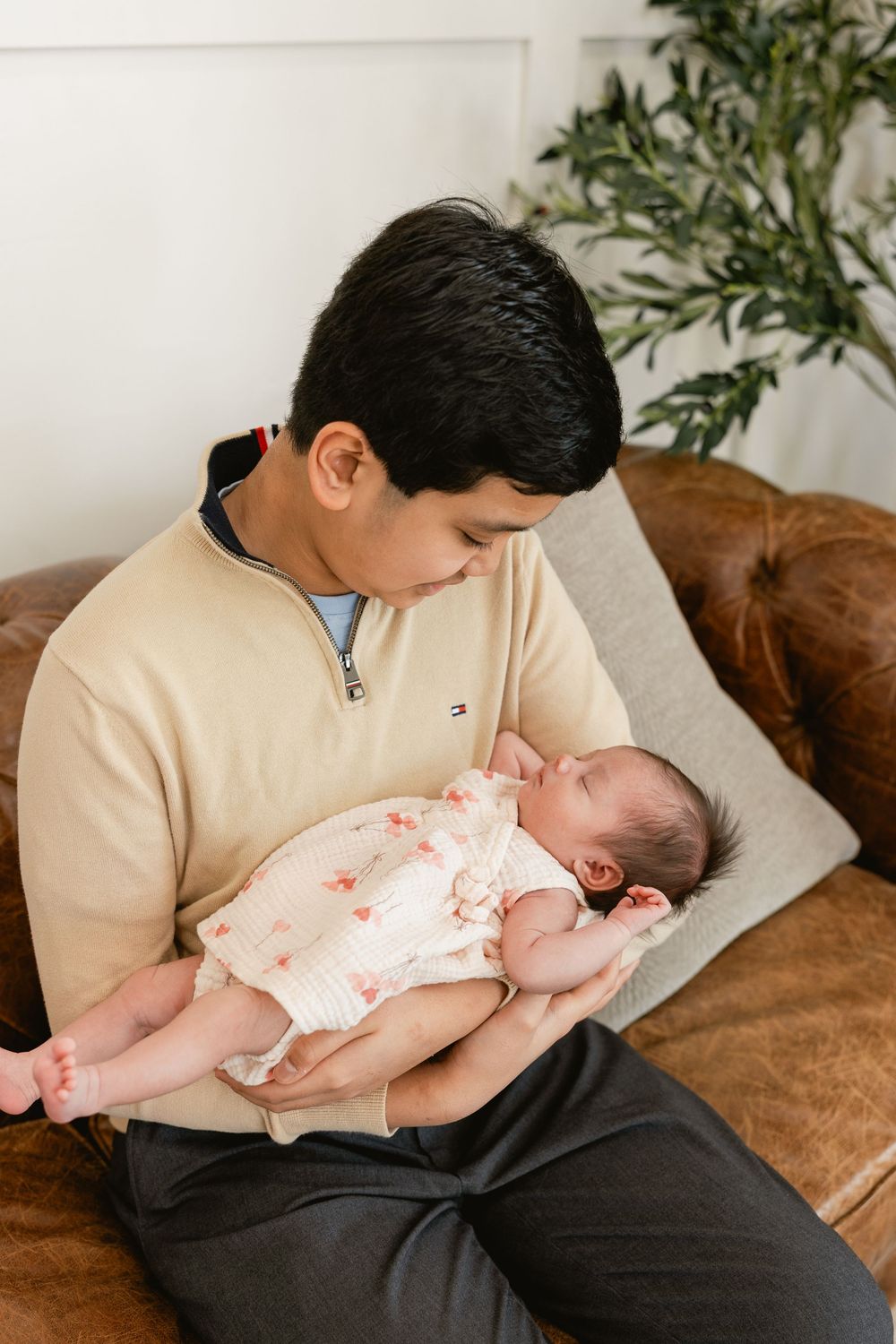 A sleeping infant in a floral outfit rests on a brown leather couch.