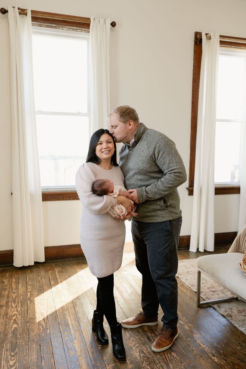 Couple in cozy sweaters sharing an intimate dance moment in a sunlit room with wooden floors.