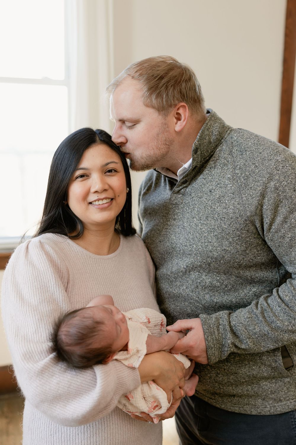 Tender embrace between couple in matching neutral sweaters near bright window.