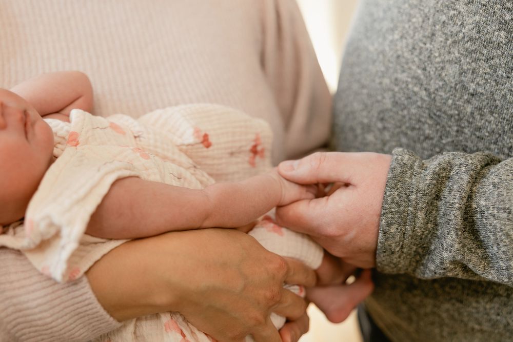 Close-up shot of hands gently holding a newborn baby wrapped in soft fabric.