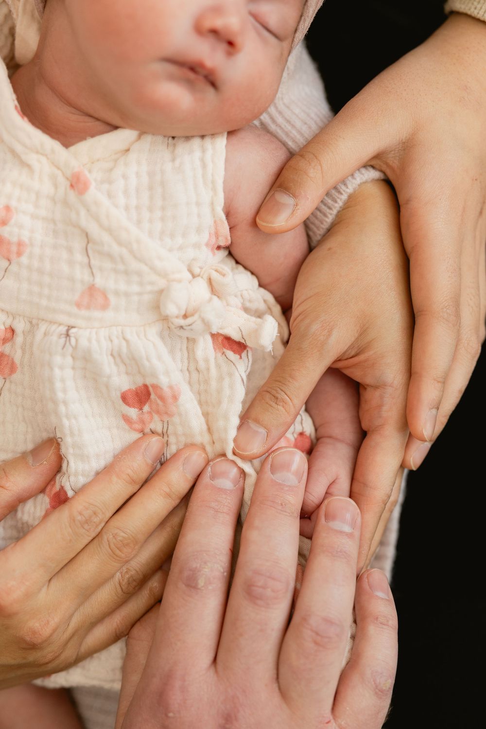 A close-up series of hands gently massaging a baby's tiny fingers and palm against a soft white textured background.